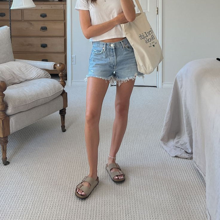 Woman wearing casual denim shorts and comfortable sandals in a cozy bedroom setting